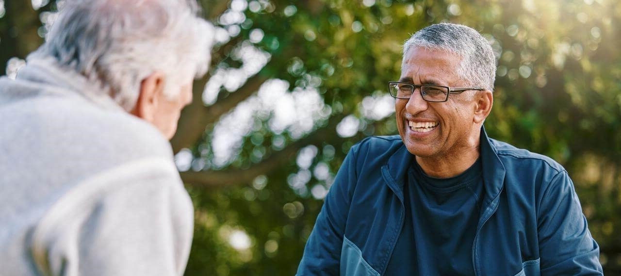 Attractive middle aged Caucasian woman with loose gray hair and wrinkles spending day indoors, leaning on white wall and smiling at camera.