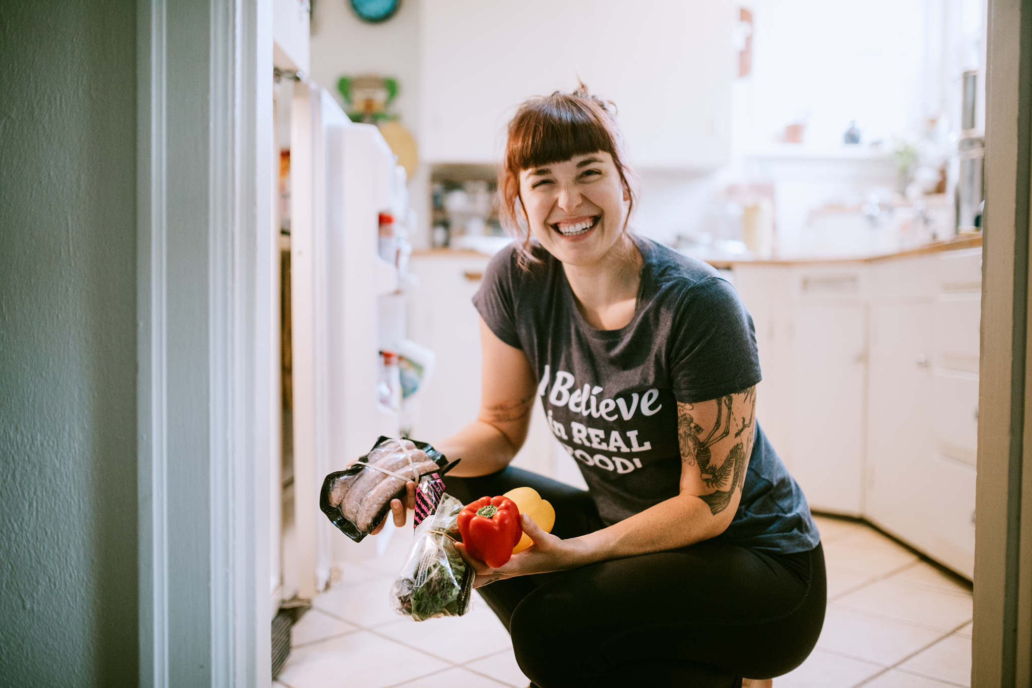A smiling woman takes some vegetables and meat from the fridge for preparing a meal.
